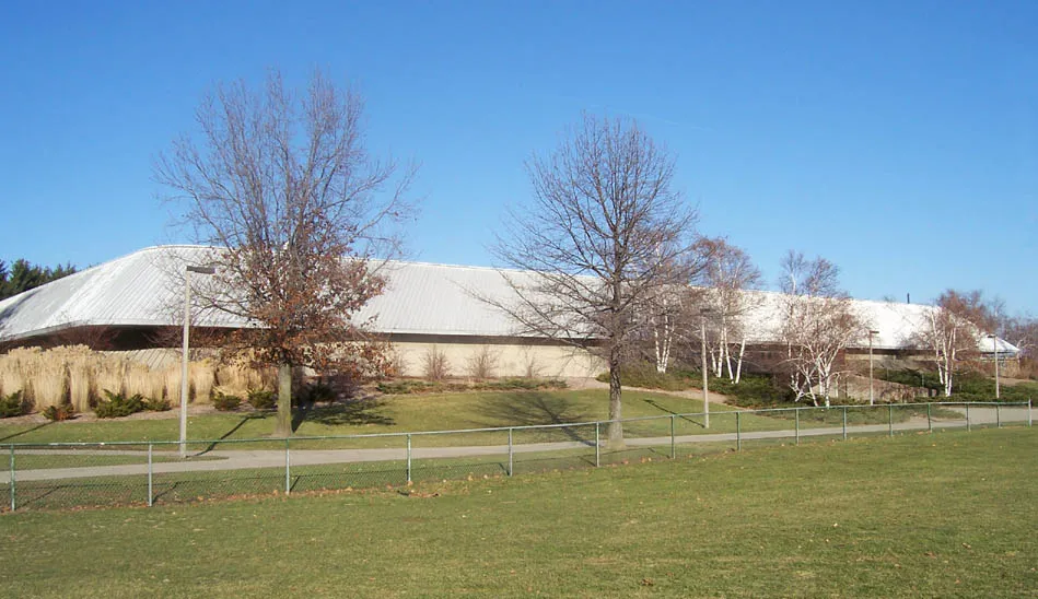 The arena's pale roof rising above a grassed bank on the Michigan State campus, seen across lawn and bare trees. — Munn Ice Arena