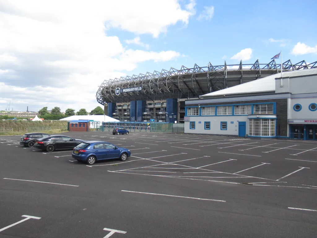 The Art Deco front of the ice rink with its round windows, beside the Murrayfield Stadium stand and the car park. — Murrayfield Ice Arena