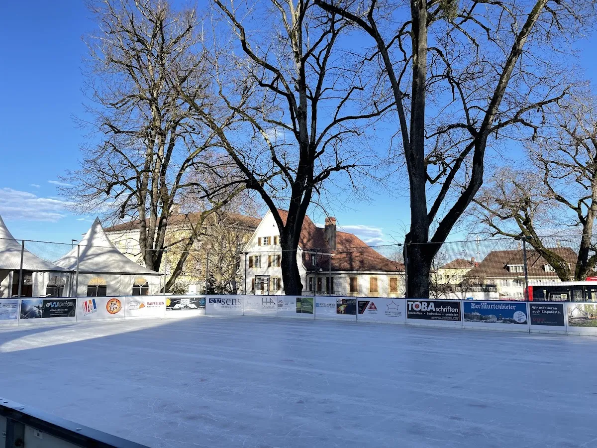 The ice field of Murten on Ice at the Berntor, with the boards, white tents and bare trees behind — Murten on Ice
