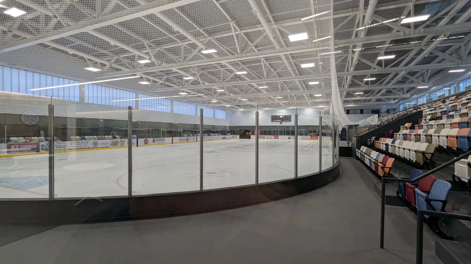 The Muskoka Lumber Arena ice seen from the lobby level, with multicoloured seats rising along the far side. — Muskoka Lumber Community Centre (Bracebridge)