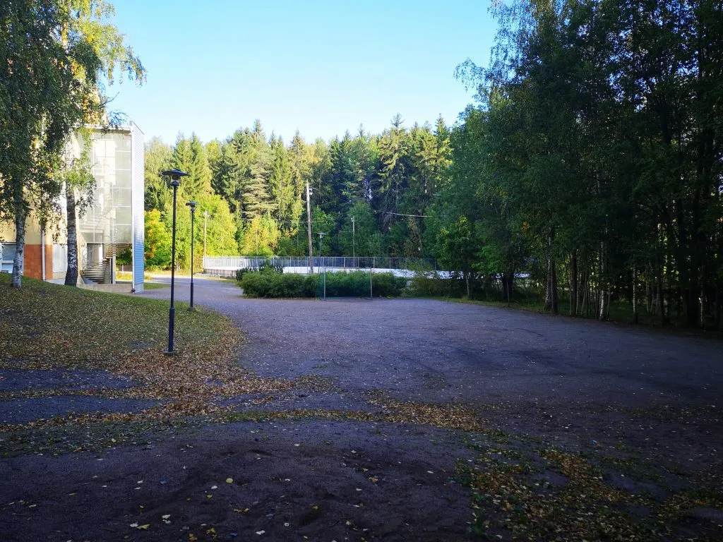 Halikon Mustamäen luistelukenttä syksyllä, puiden ympäröimä asfalttialue ja taustalla kentän aita. – Mustamäen kaukalo (Salo)
