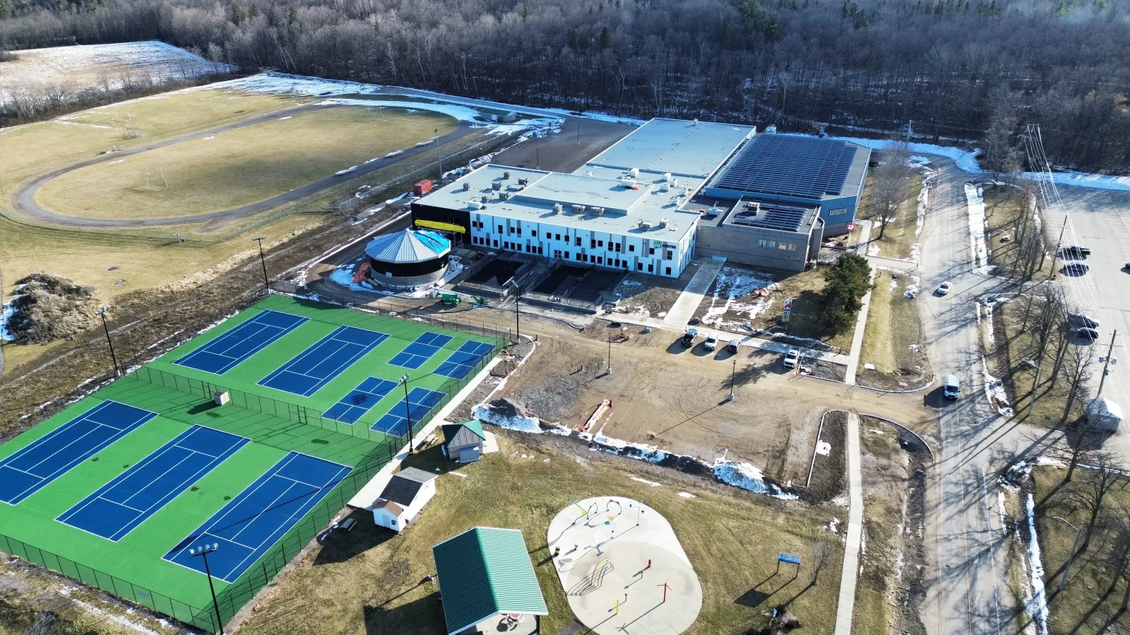 Una vista aérea del myFM Centre Recreation Complex con su nueva ampliación frontal, las canchas de tenis y pickleball y el estacionamiento junto al camino. — myFM Centre (Renfrew)