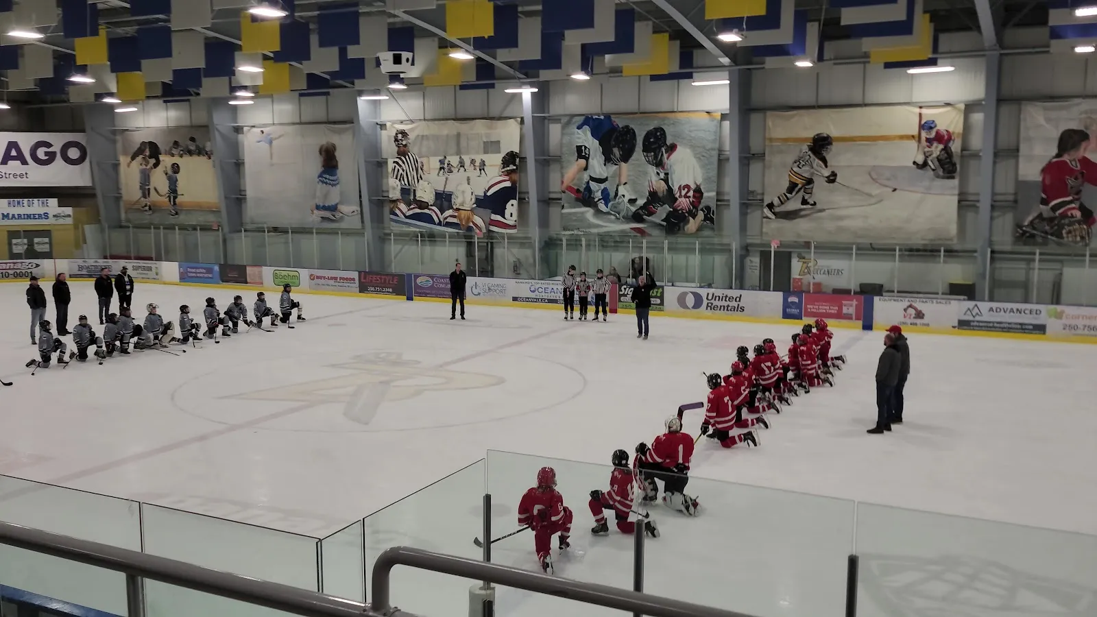 Nanaimo Ice Centre rink with players kneeling at centre ice, seen from the stands — Nanaimo Ice Centre