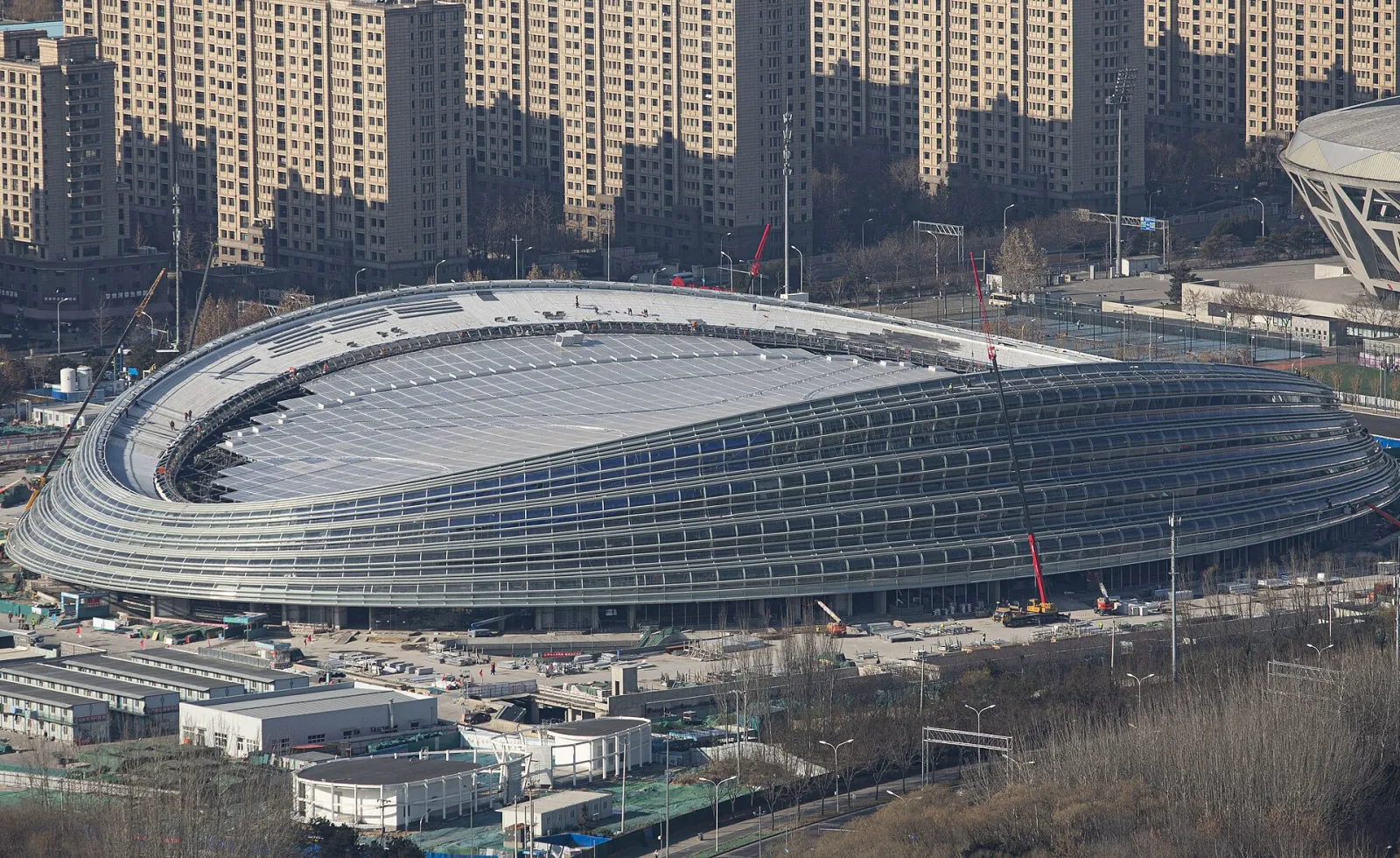 The National Speed Skating Oval, the Ice Ribbon, seen from the north-east with its glass facade of curved panels and the roof — National Speed Skating Oval