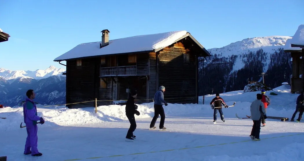 Skaters and players on the natural ice field at Obermutten in front of a timber chalet — Natureisfeld Obermutten