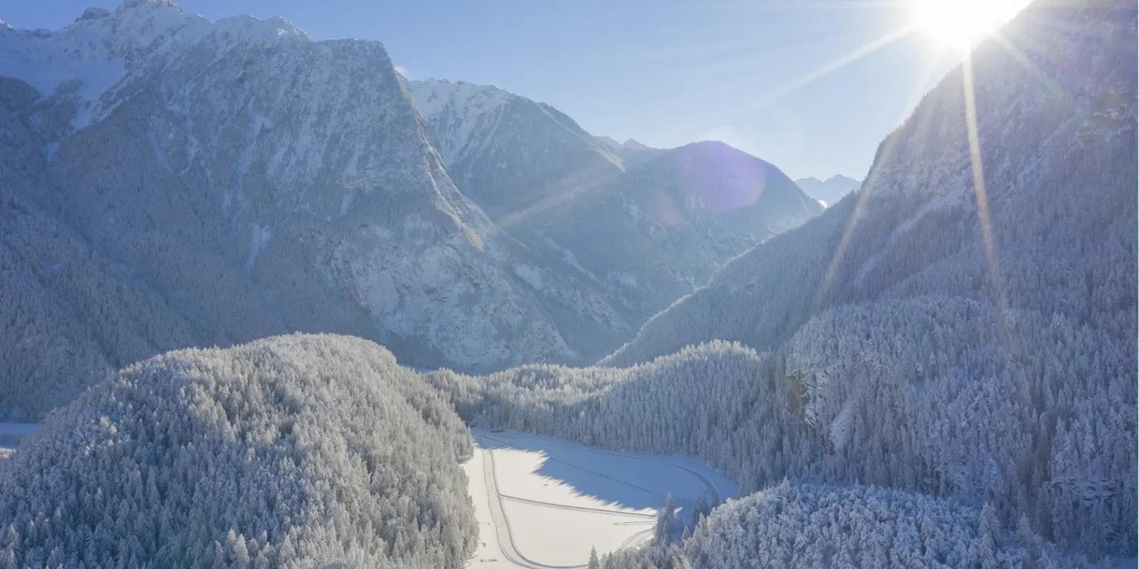 Aerial view of the Piburger See in winter, with the groomed skating track on the ice of the lake in a snowy mountain valley. — Natur-Eisfläche Piburger See