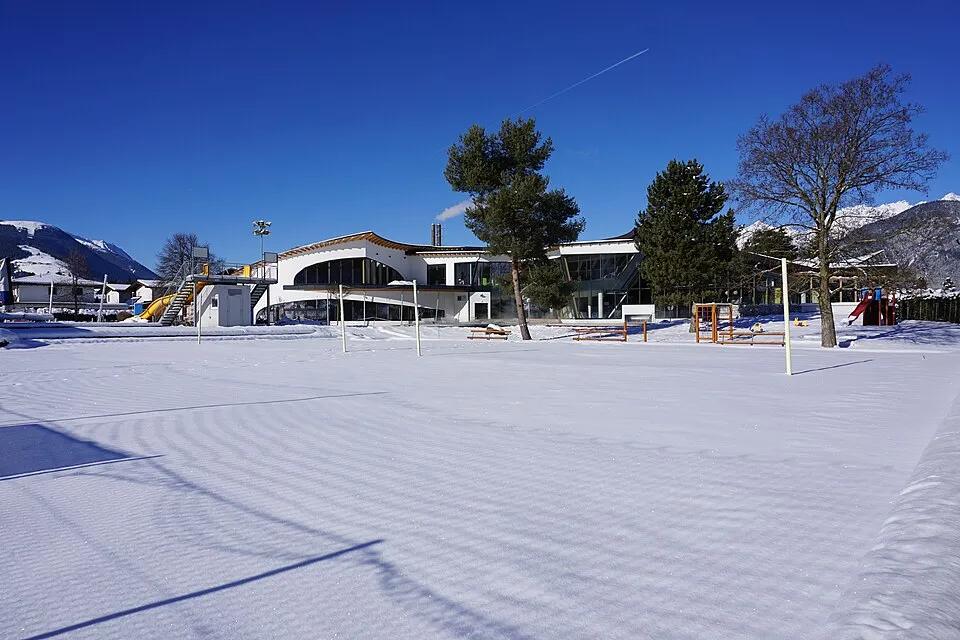 The Freizeitzentrum Axams, with its outdoor pool area under snow, seen across the lawn — Natureislaufplatz Freizeitzentrum Axams