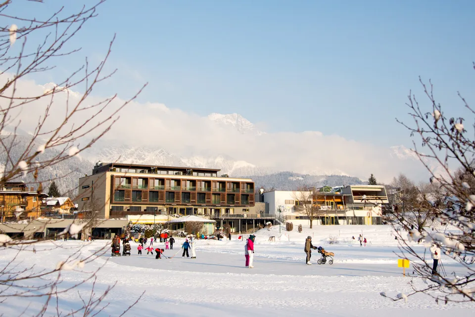 Skaters and walkers spread across the frozen Ritzensee in Saalfelden, with a modern lakeside hotel beyond the ice. — Natureislaufplatz Ritzensee