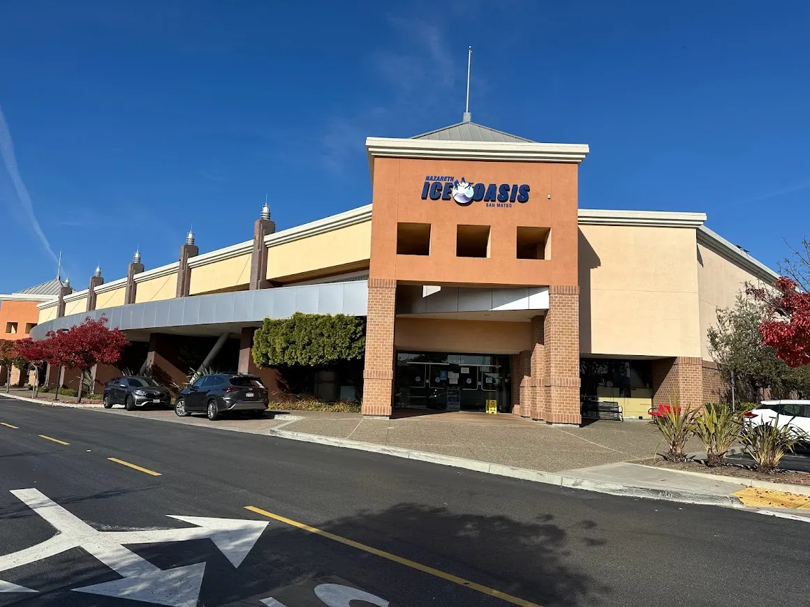 The Bridgepointe entrance: a terracotta tower with the blue ICE OASIS sign above the doors, beside a low row of storefronts. — Nazareth Ice Oasis