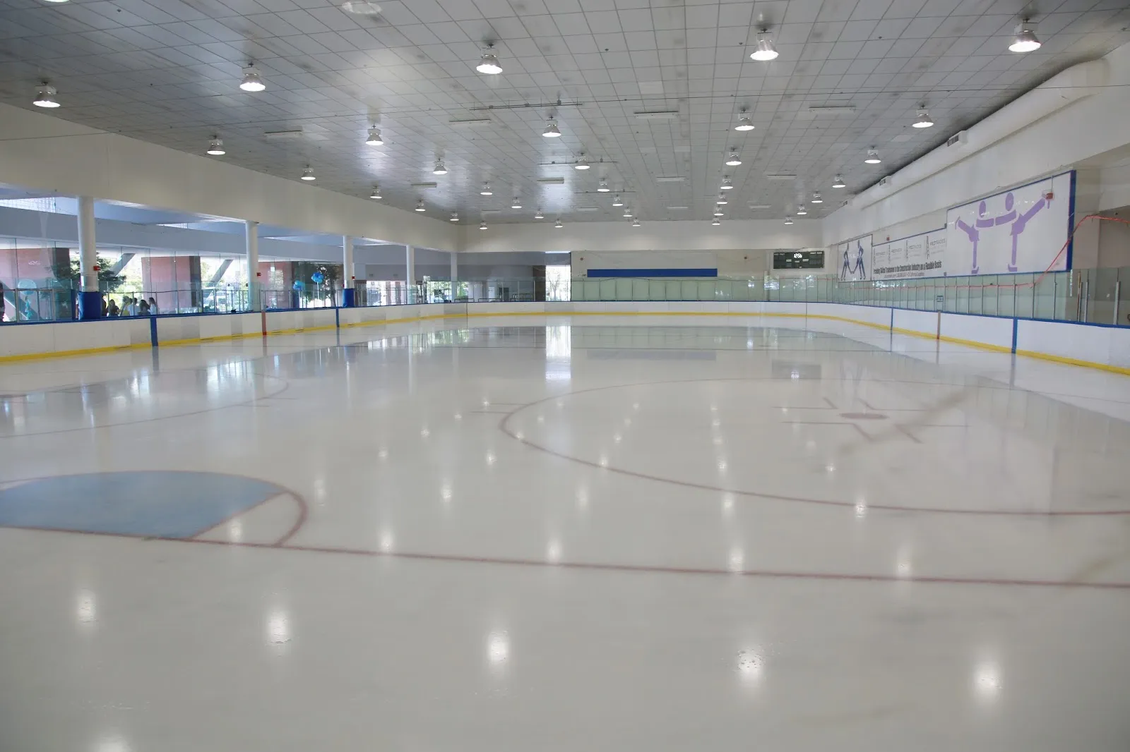 The empty sheet under rows of ceiling lights, with the glass and boards running down both sides. — Nazareth Ice Oasis