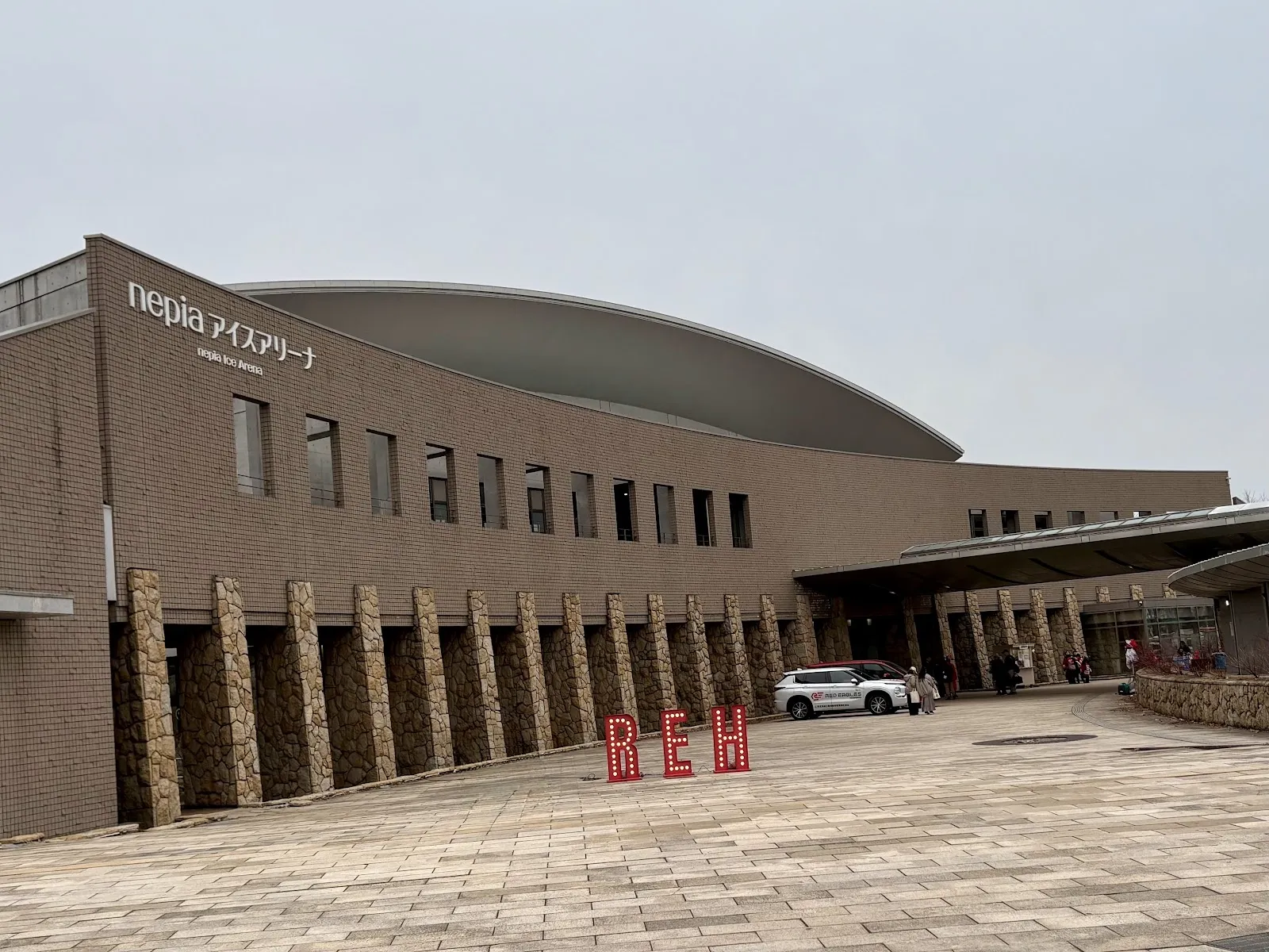 The domed front of the nepia Ice Arena in Tomakomai seen across the car park under an overcast sky. — nepia Ice Arena (Hakucho Arena)