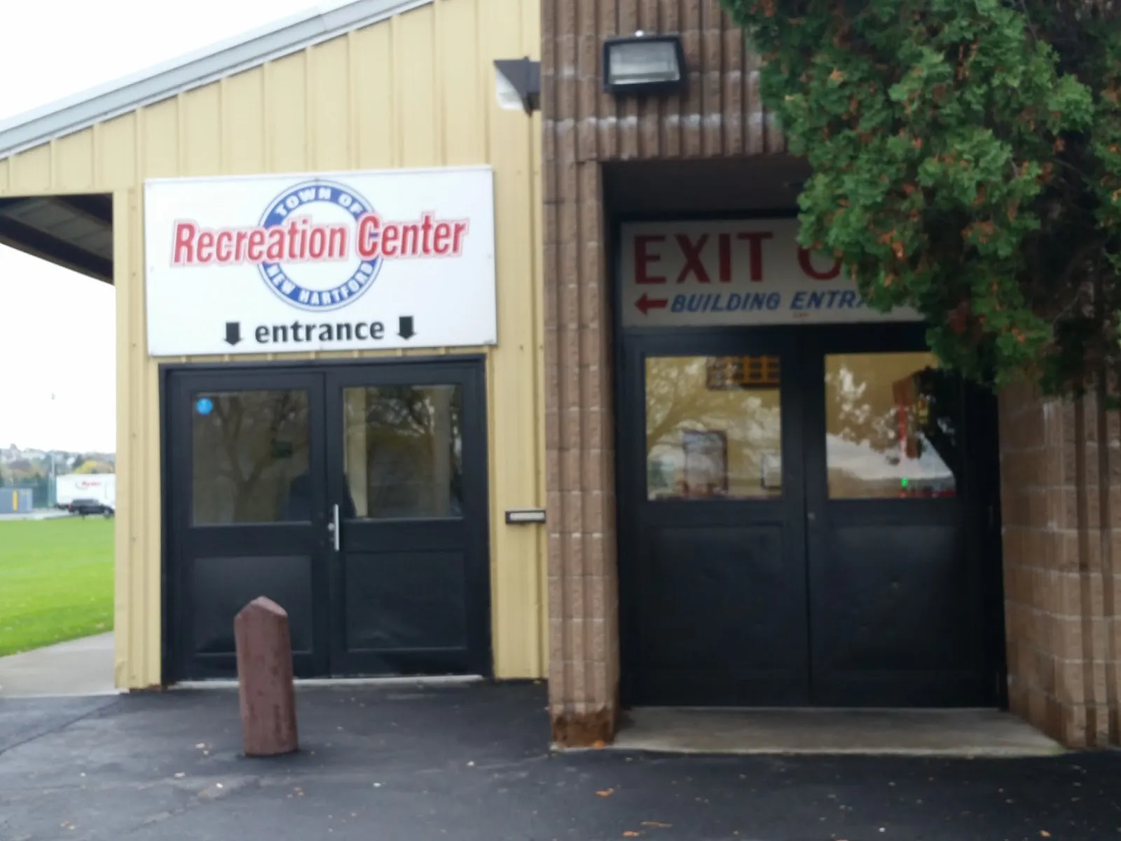 The Recreation Center entrance: black double doors under a Town of New Hartford Recreation Center sign on a tan metal-sided building. — New Hartford Recreation Center