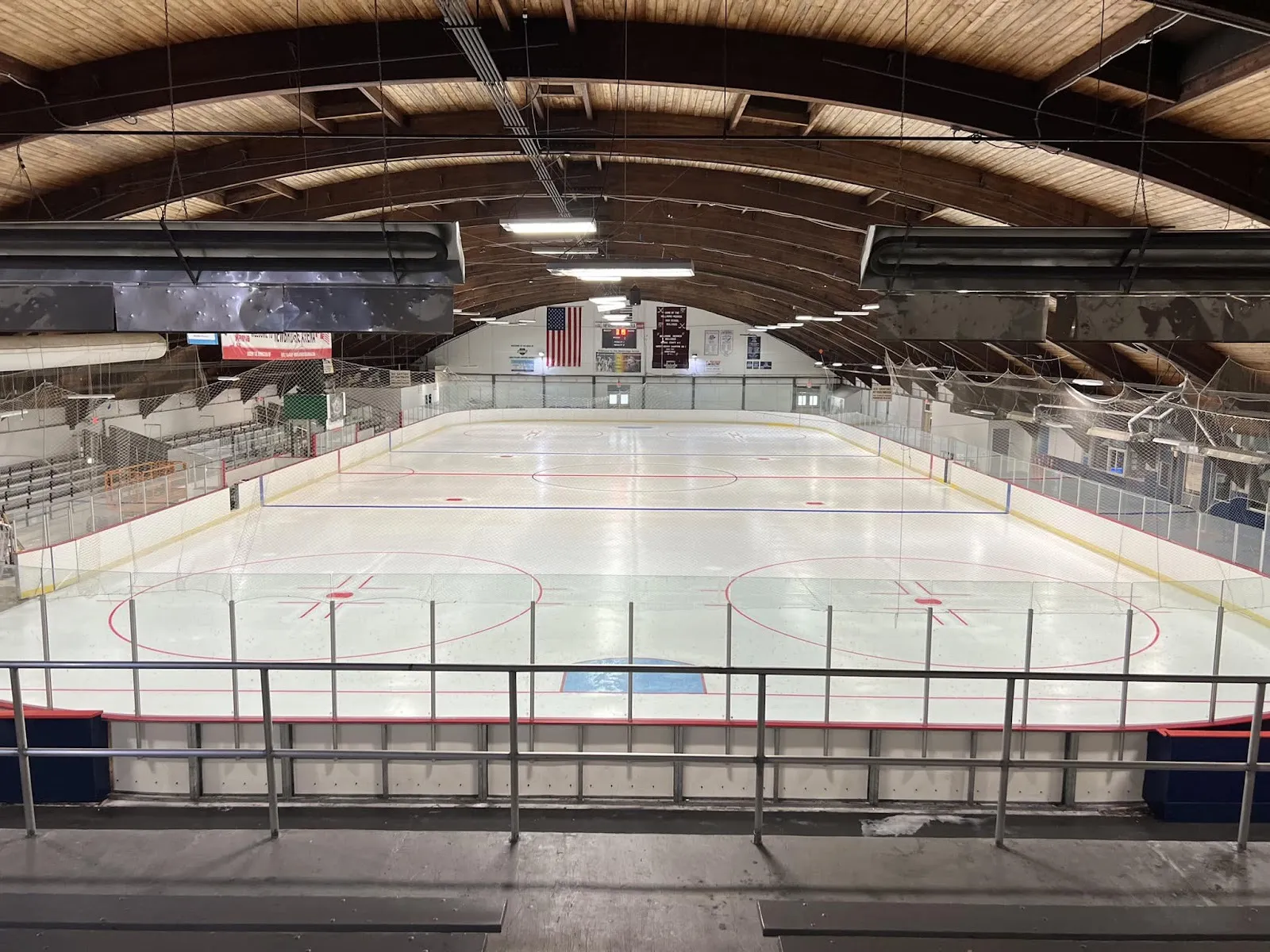 La pista vacía de Newbridge Arena desde las gradas, con líneas recién pintadas bajo un techo de madera en arco y banderas en el extremo opuesto — Newbridge Arena