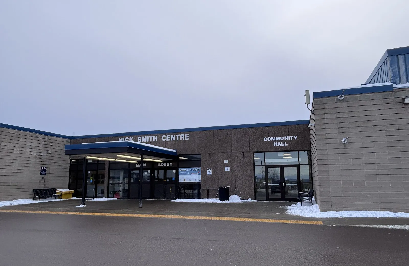 The Nick Smith Centre's brown brick front with its name above the main lobby canopy and the community hall doors, in light snow. — Nick Smith Centre