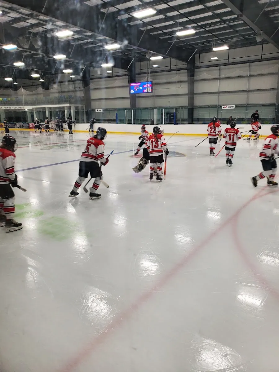 A team skating away from the camera across the ice at Niverville Centennial Arena, with the roof trusses and scoreboard behind. — Niverville Centennial Arena