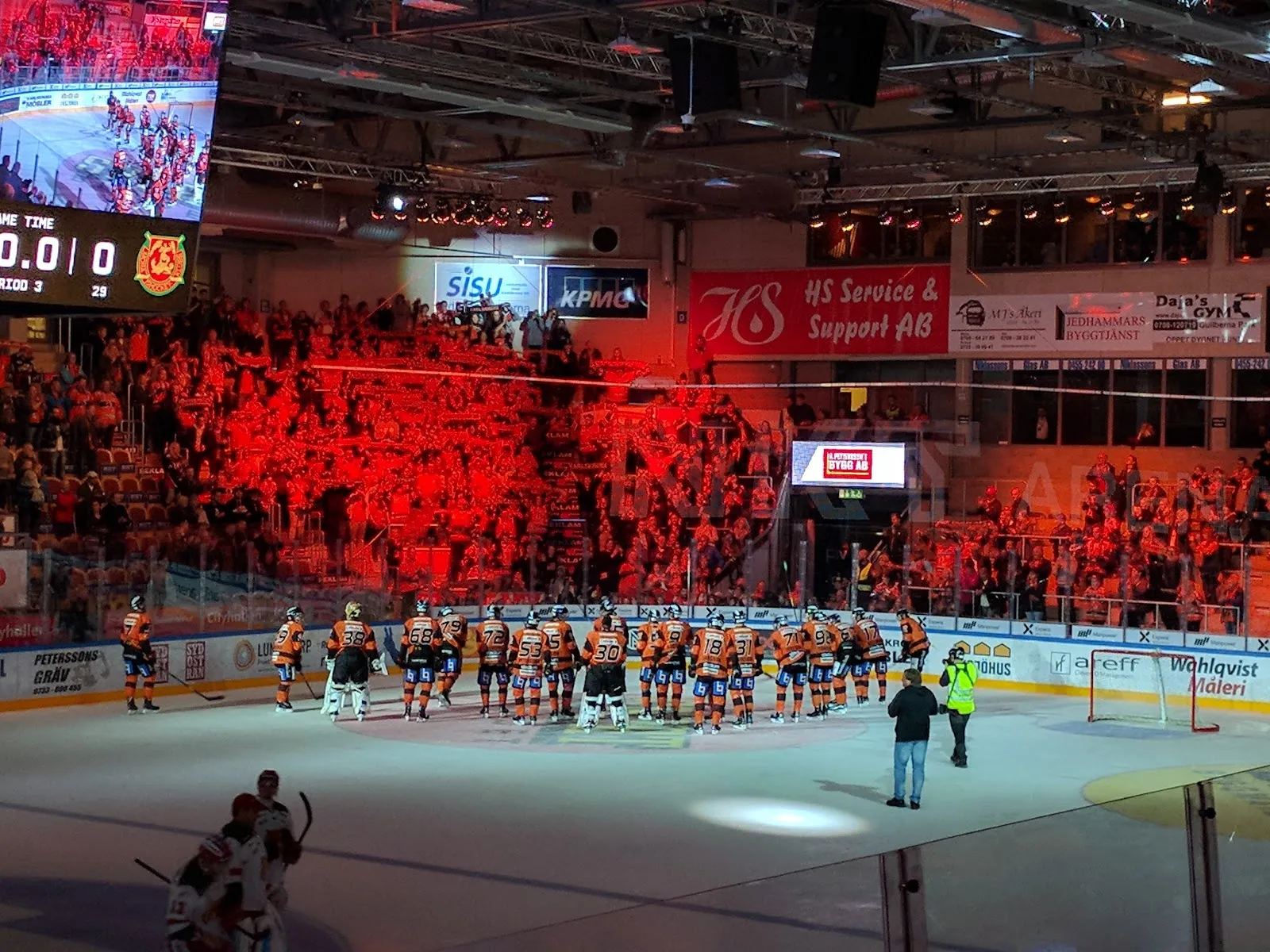 The ice of Arena Karlskrona during a match, with the home crowd in red filling the stands behind the boards and the scoreboard above. — NKT Arena