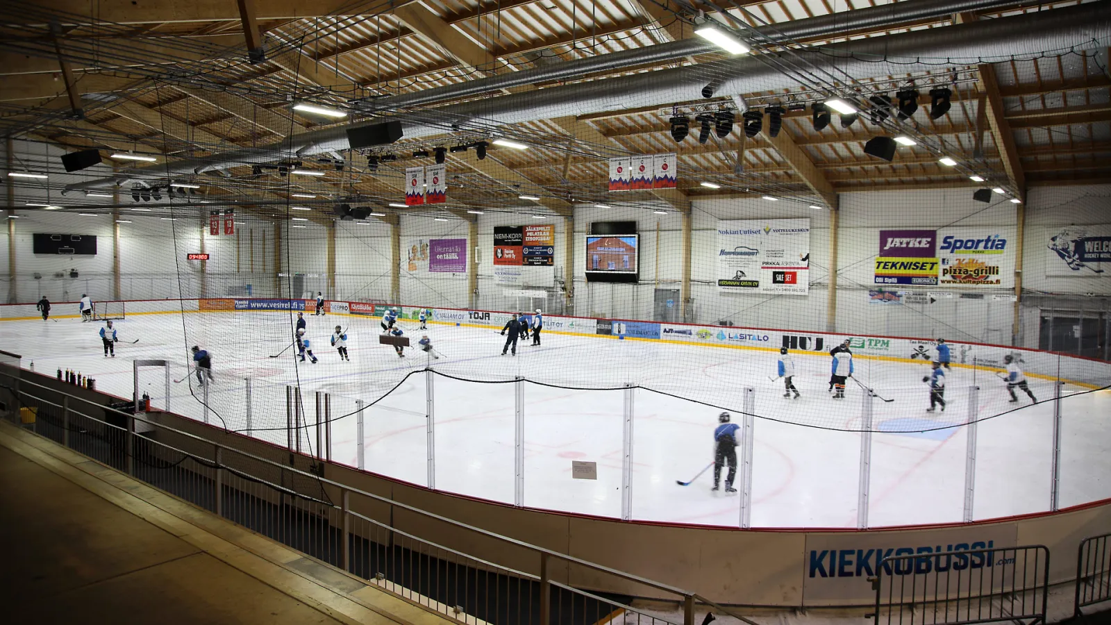 The ice of the main hall (Kilpahalli) at Nokian jäähalli with a practice in progress, players spread across the rink under the timber-beamed roof and sponsor boards — Nokian jäähalli