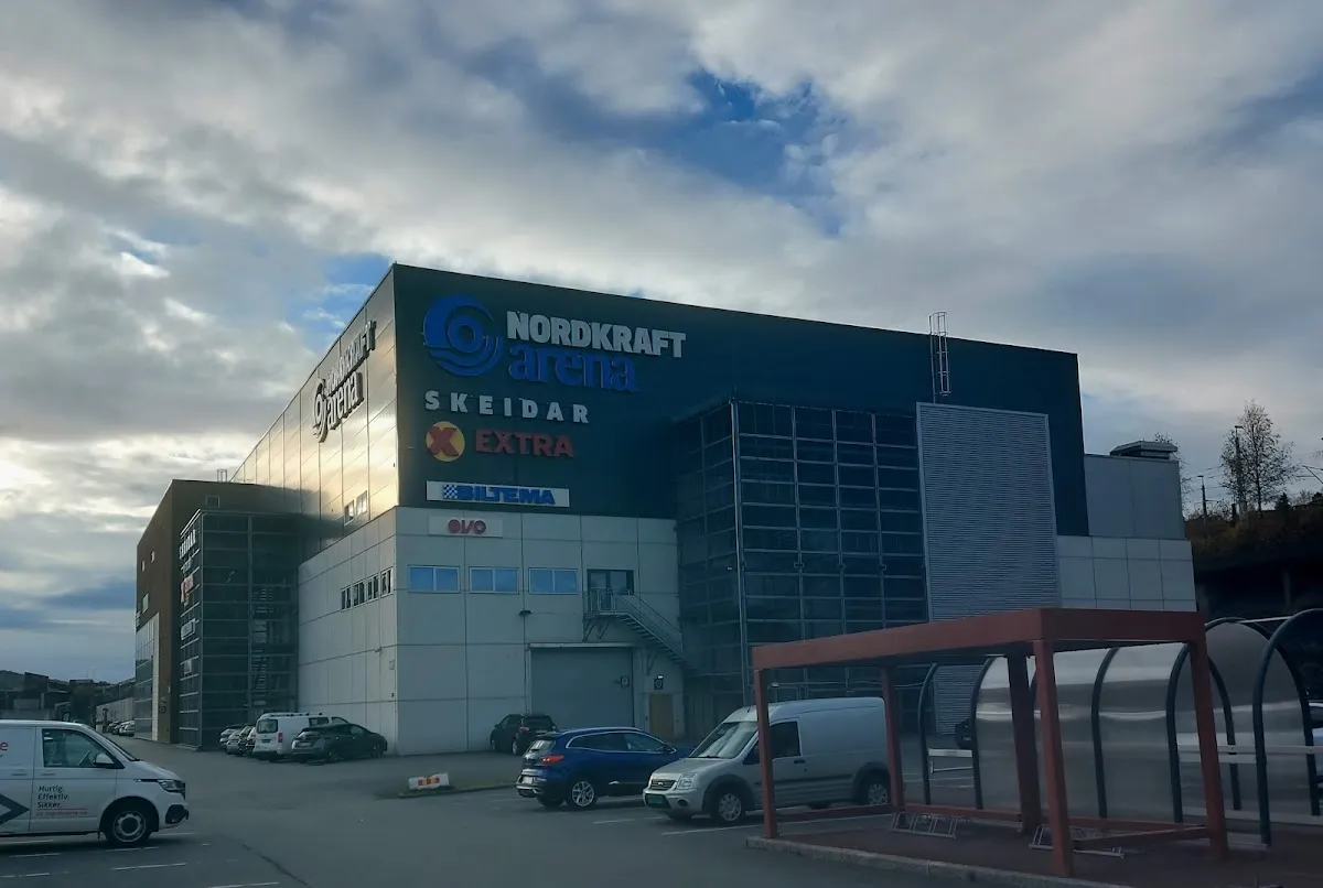 Arenaens hjørneinngang av glass og metall under Nordkraft Arena-skiltet, sett fra parkeringsplassen. — Nordkraft Arena