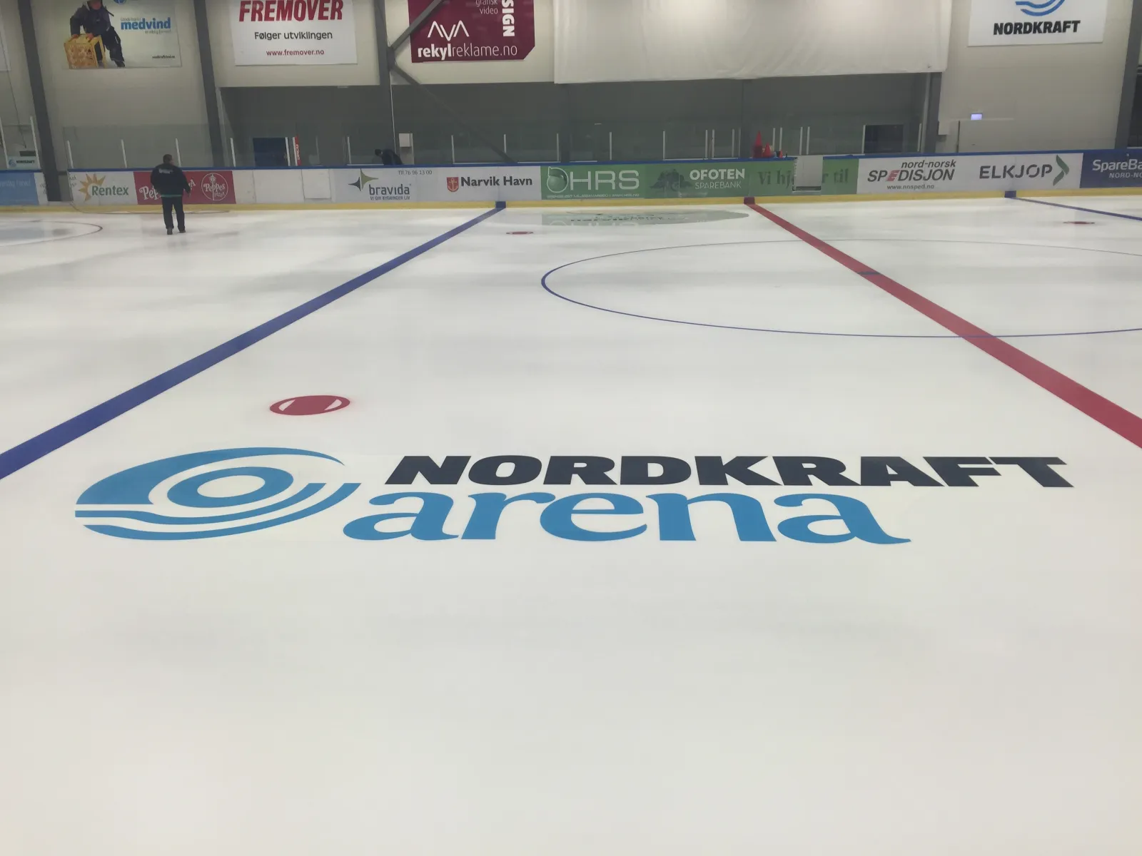 Den tomme isen i Nordkraft Arena med blå linjer, avkastsirkel og arenaens logo malt midt på isen. — Nordkraft Arena