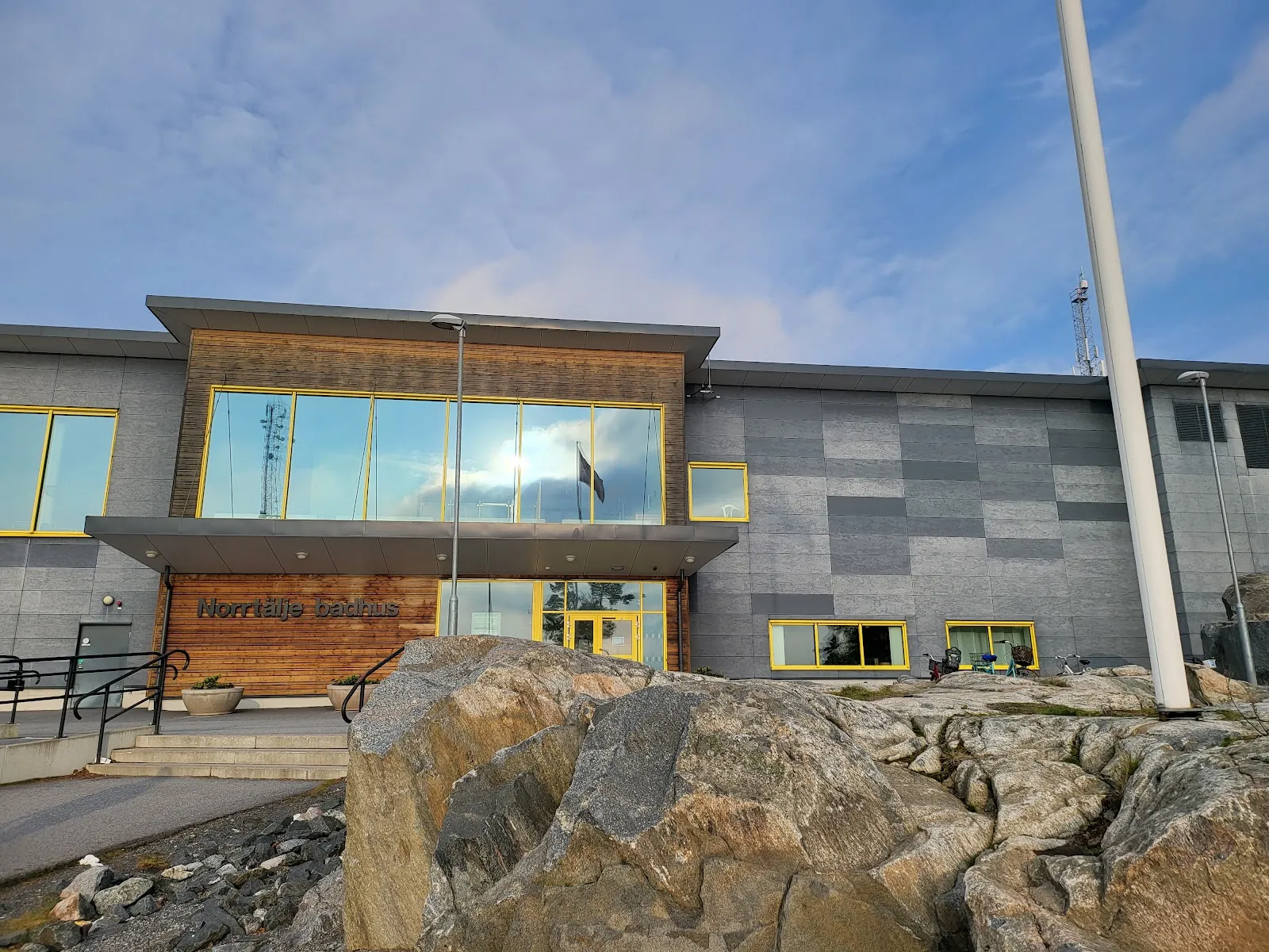 The entrance of Norrtälje Sportcentrum, a grey and timber building with yellow window frames and its name on the front — Norrtälje Sportcentrum