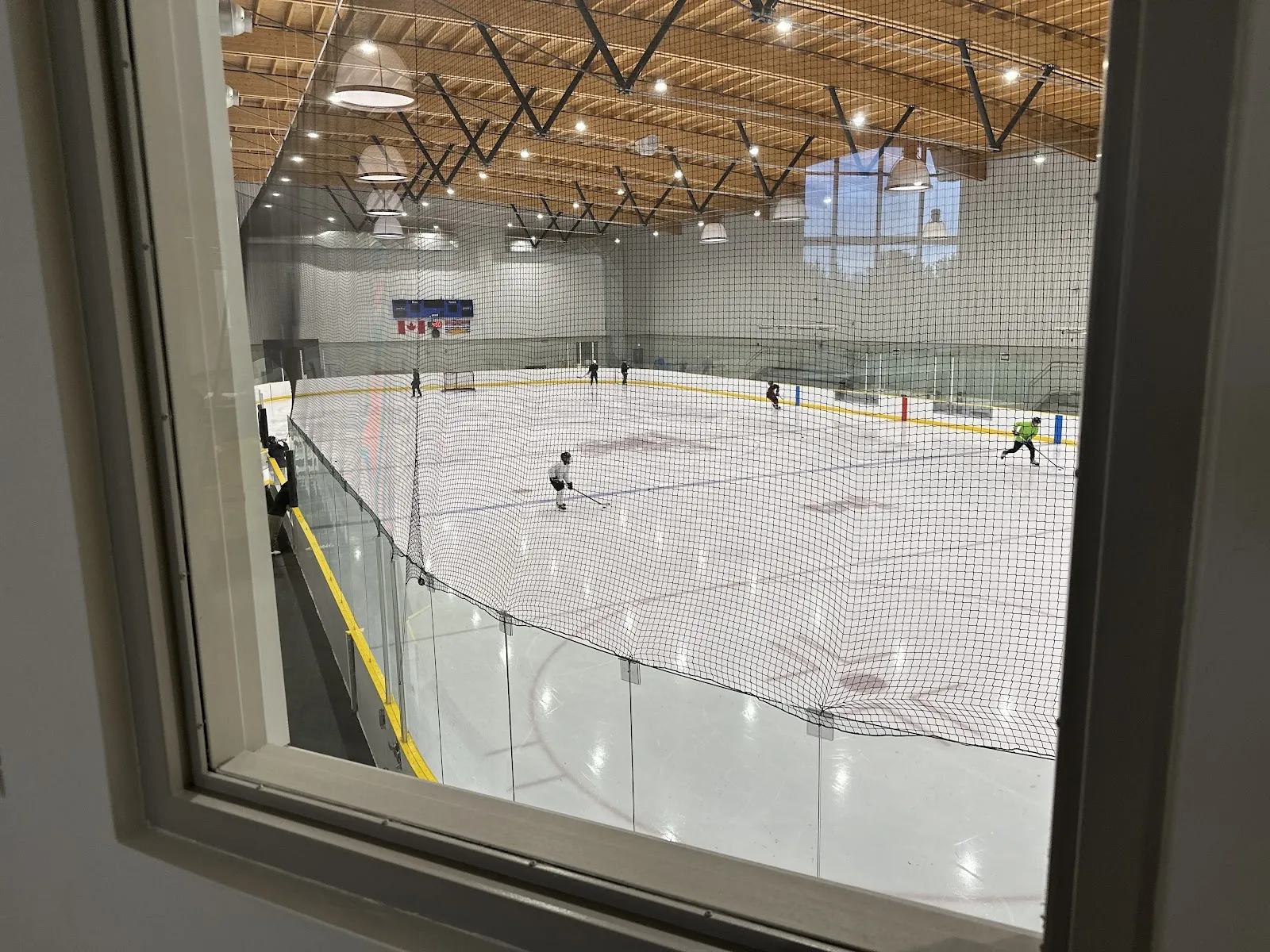 North Delta Recreation Centre: players on the arena ice seen through a viewing window — North Delta Recreation Centre