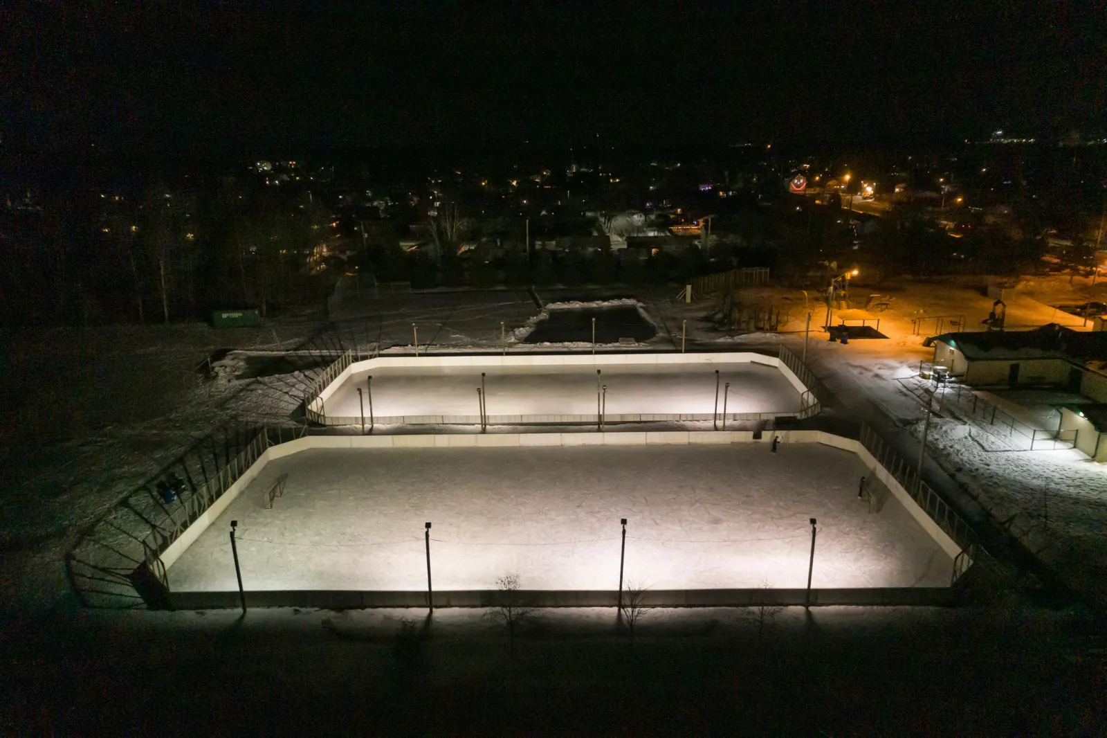 Las pistas con vallas del North End Community Centre iluminadas de noche, vistas desde arriba — North End Community Centre Outdoor Rinks