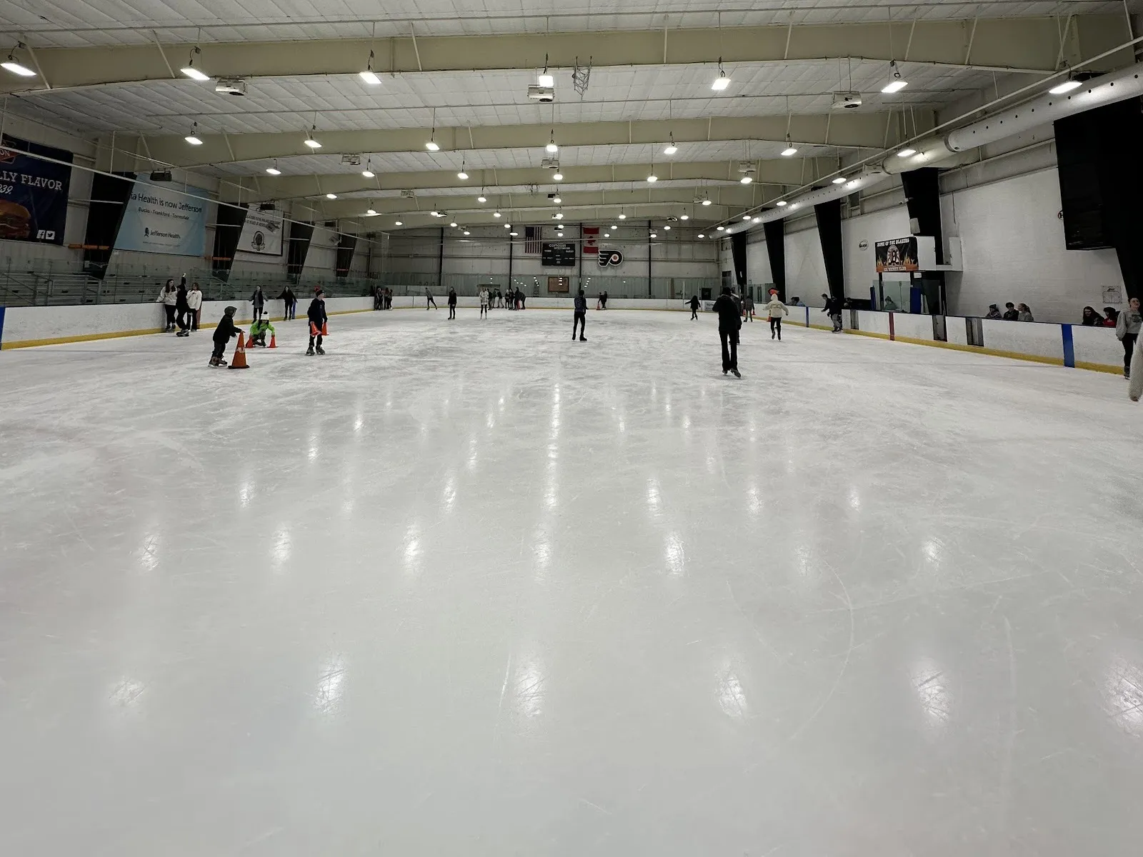 Public skating on a Northeast Skate Zone sheet, the long rink under white roof beams with the Flyers logo and scoreboard at the far end — Northeast Skate Zone