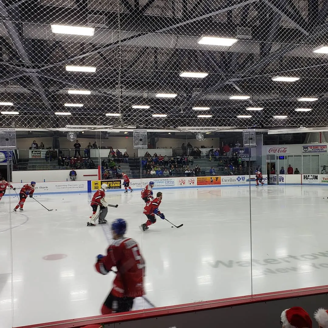 A hockey game on the ice sheet at Watertown Municipal Arena seen through the boards glass — Northern Credit Union Community Arena