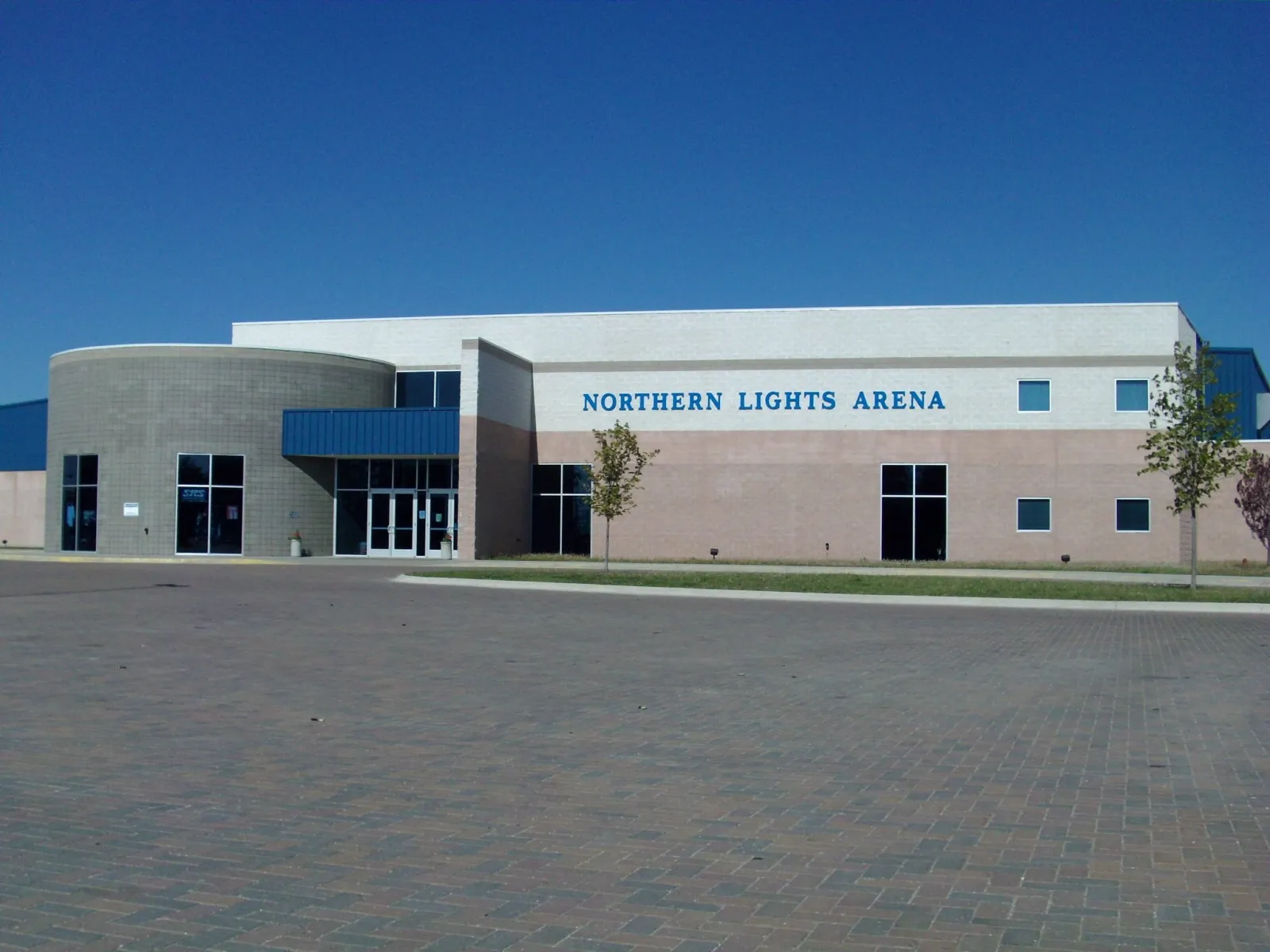 El edificio de Northern Lights Arena en Alpena con su nombre sobre la entrada, visto al otro lado de la explanada pavimentada — Northern Lights Arena