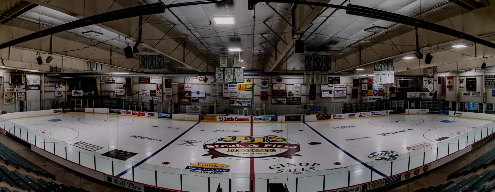 Vista amplia con ojo de pez del hielo vacío de Northern Lights Arena en Alpena desde el nivel de la pista, con las vallas y el logotipo del centro del hielo — Northern Lights Arena