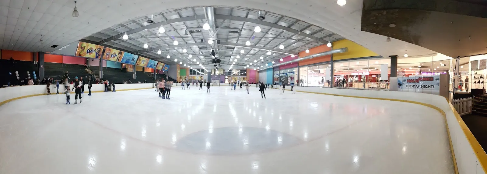 A wide view of the Northgate Ice Rink ice sheet with the mall's shop fronts around it and only a few skaters — Northgate Ice Rink