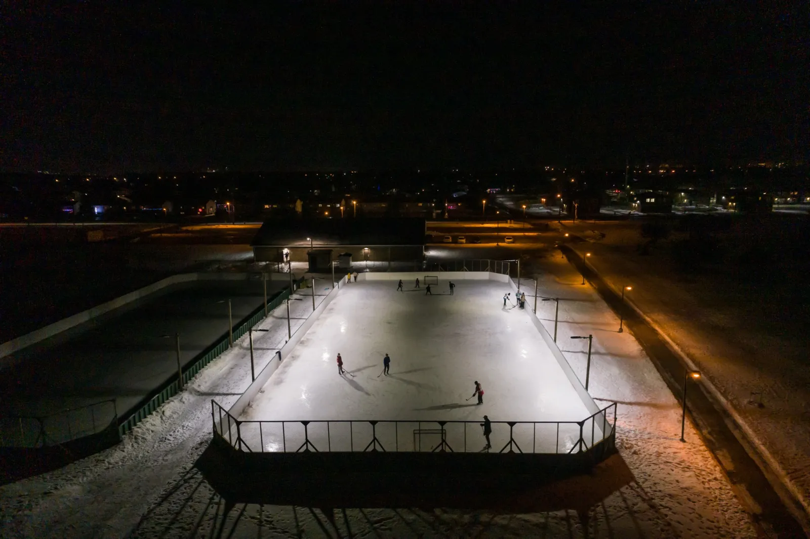 La pista con vallas de Northwood Playfield iluminada de noche, vista desde arriba, con patinadores en el hielo — Northwood Playfield Outdoor Rinks