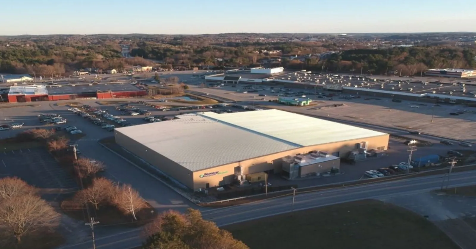 Aerial view of the tan metal-sided Norway Savings Bank Arena building with its sign over the entrance, parking lots on both sides, and Turner Street in the foreground. — Norway Savings Bank Arena