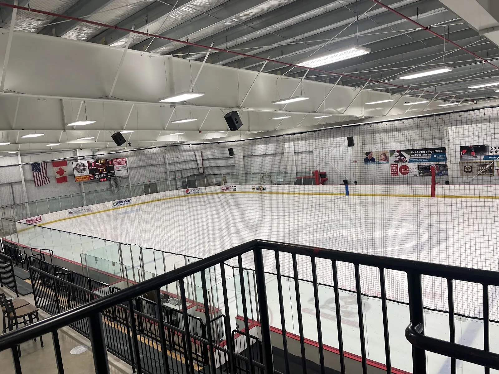An empty rink at Norway Savings Bank Arena from the upper stairs, netting over the glass and flags by the scoreboard — Norway Savings Bank Arena