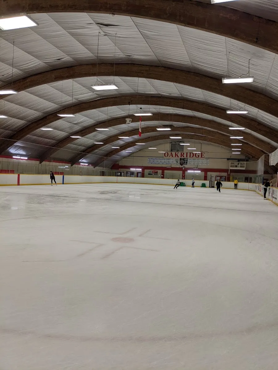 The ice under the curved wooden roof beams, with OAKRIDGE on the far wall and a few skaters at the far end. — Oakridge Arena