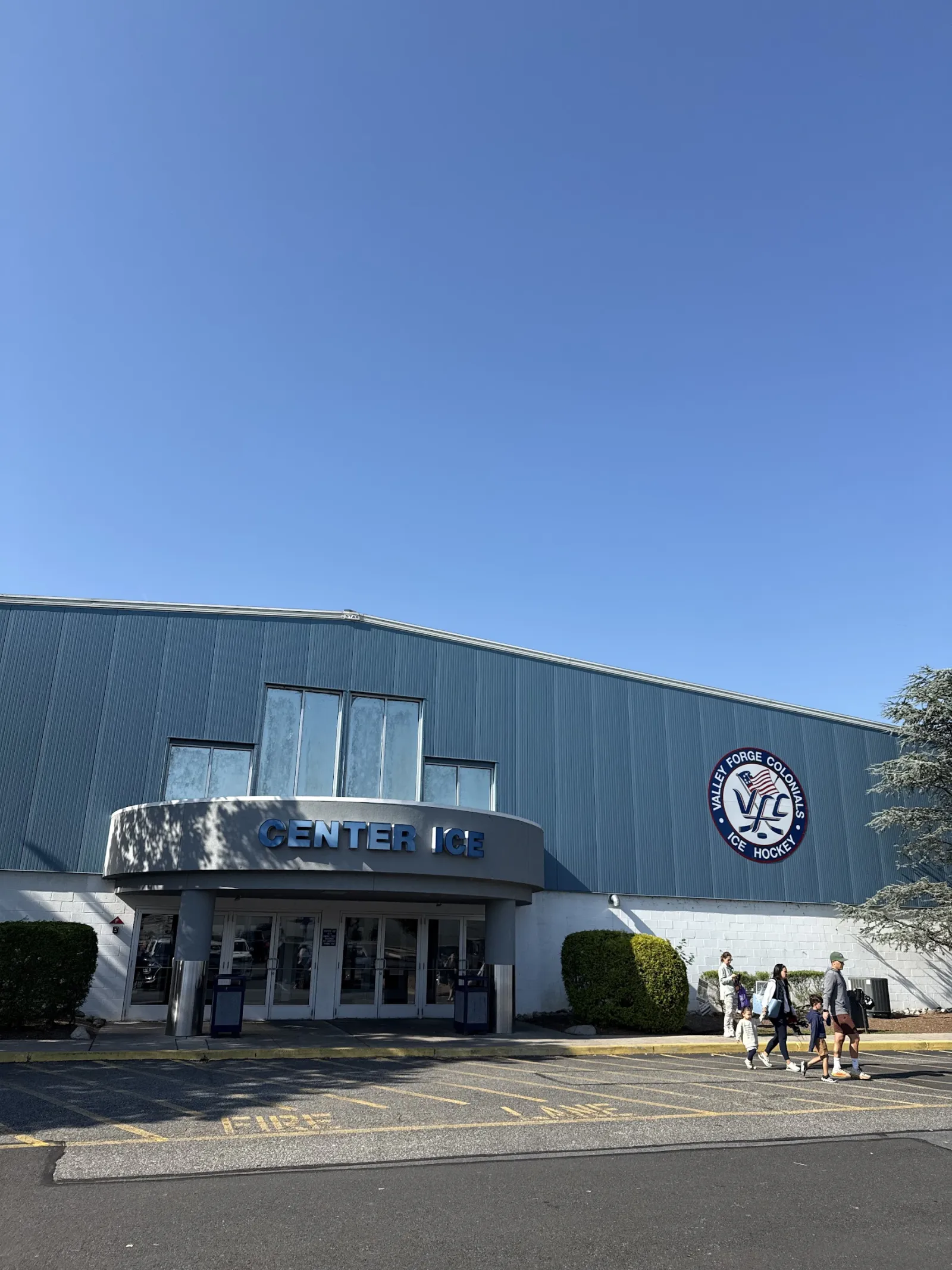 The blue metal building with a Center Ice sign over the entrance and a Valley Forge Colonials logo on the wall, under a clear sky. — Oaks Center Ice