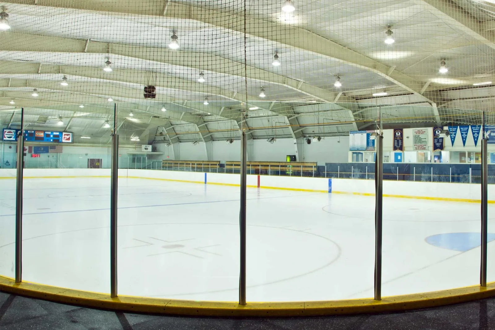 Toda la pista vacía de Maple Grove Arena, amplia vista de ojo de pez bajo un techo en arco con costillas, marcador con las marcas Pepsi/Crush/7Up, banderas de EE. UU. y Canadá y vallas con anuncios de Scotiabank y de patrocinadores locales. — Maple Grove Arena