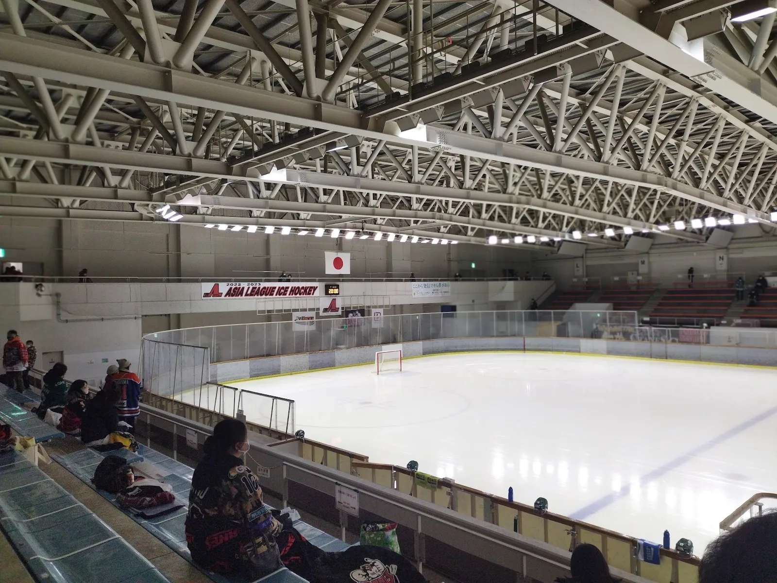 The ice sheet inside Obihiro Forest Ice Arena seen from the stands, with the steel roof trusses overhead and the boards around the ice. — Obihiro Forest Ice Arena