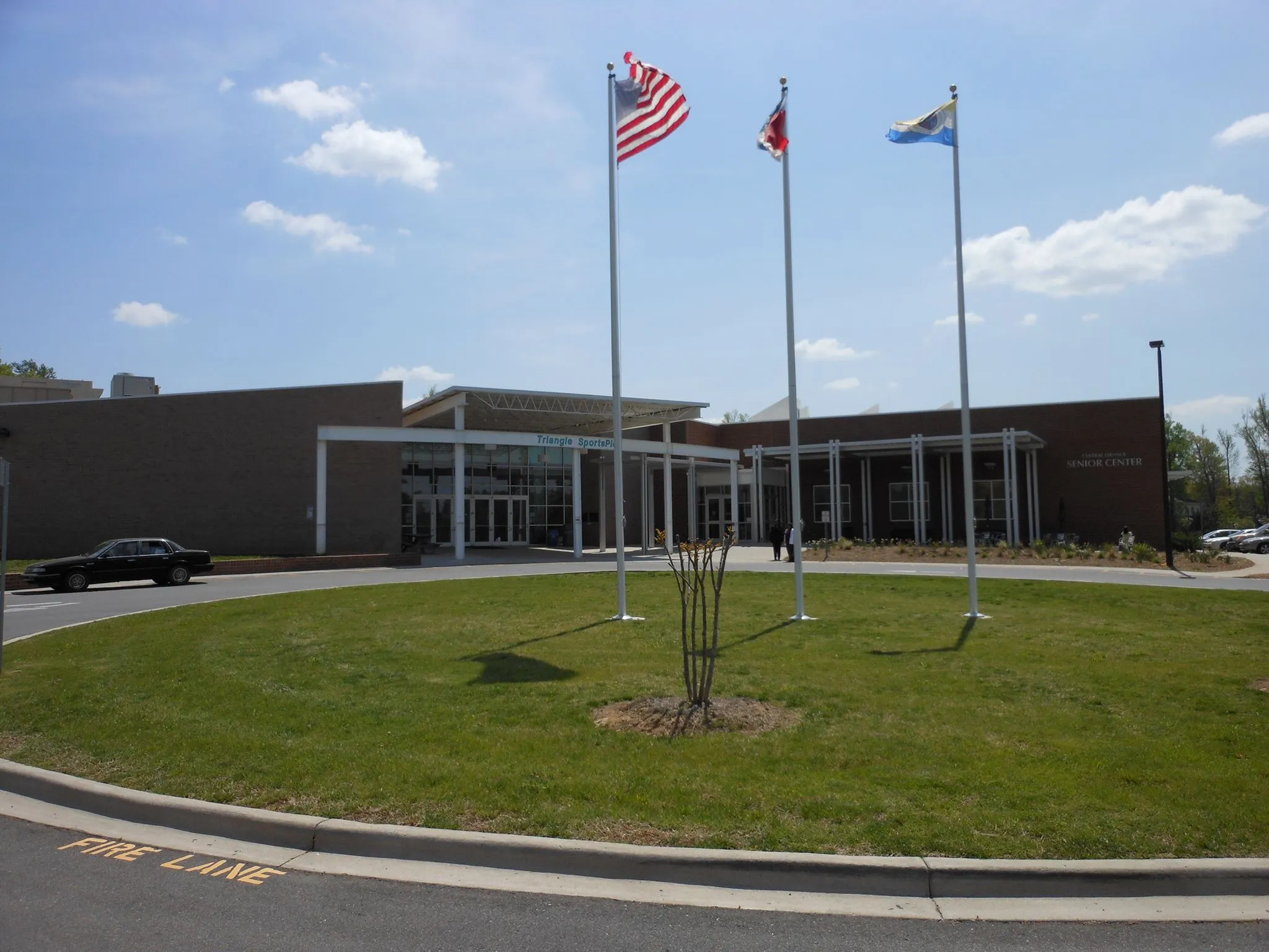 Three flagpoles on the lawn outside the entrance — Orange County Sportsplex