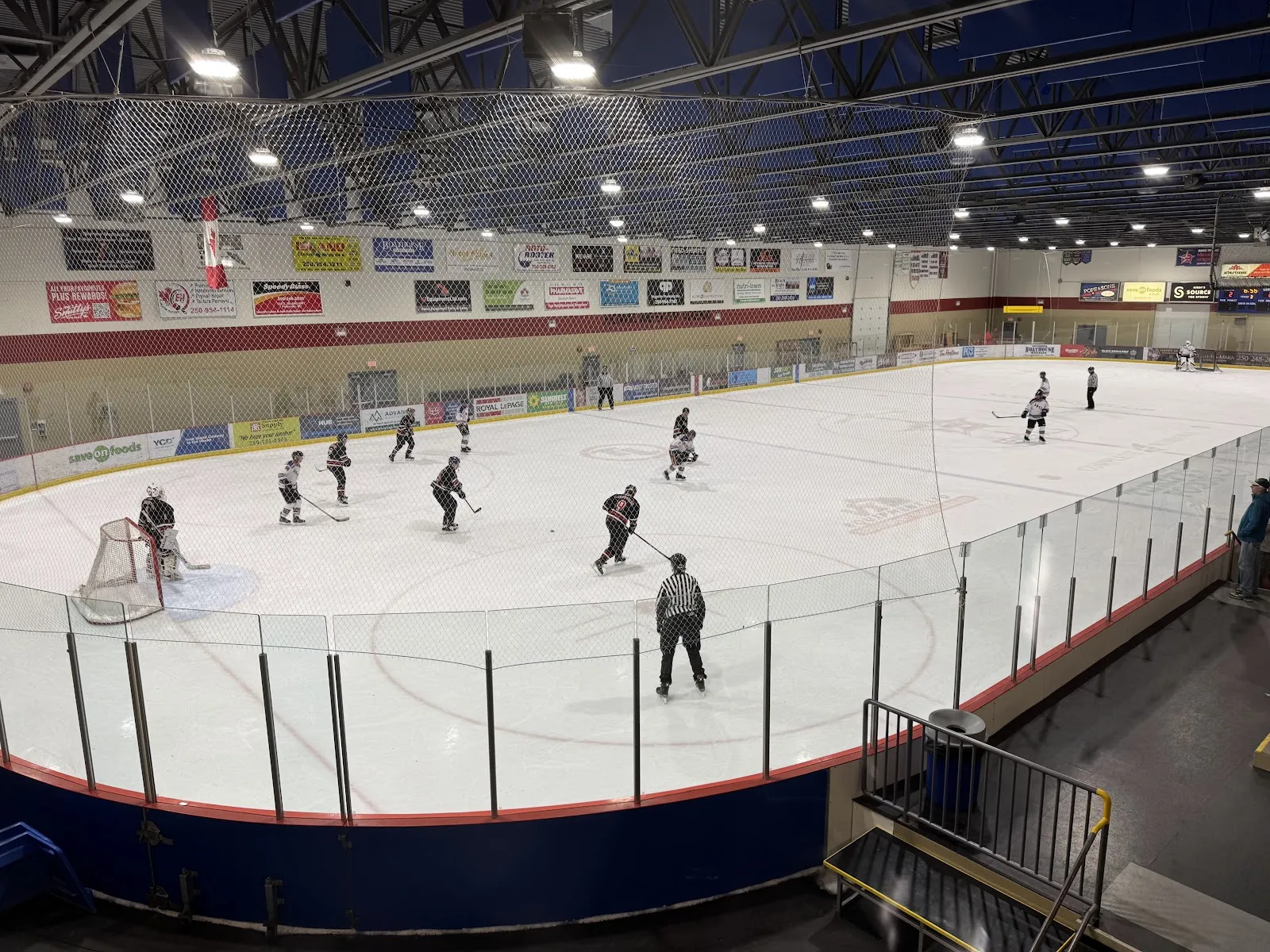 A hockey game on the main sheet at Oceanside Place Arena in Parksville, seen from the stands with the boards and sponsor banners — Oceanside Place Arena