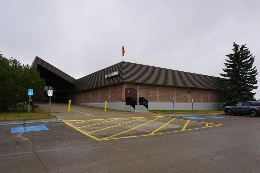 The Sportsplex's brown-roofed brick entrance wing on an overcast day, with a painted accessible-parking area in front. — Olds Sportsplex