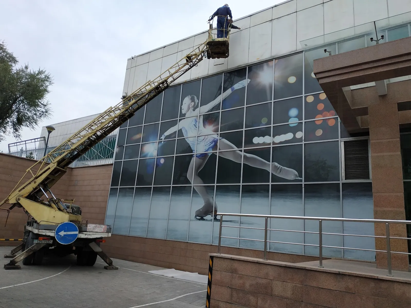 The glass facade of the Olimpic ice arena on Abay Avenue in Almaty, with a large figure skater picture across the windows — Olimpic Arena