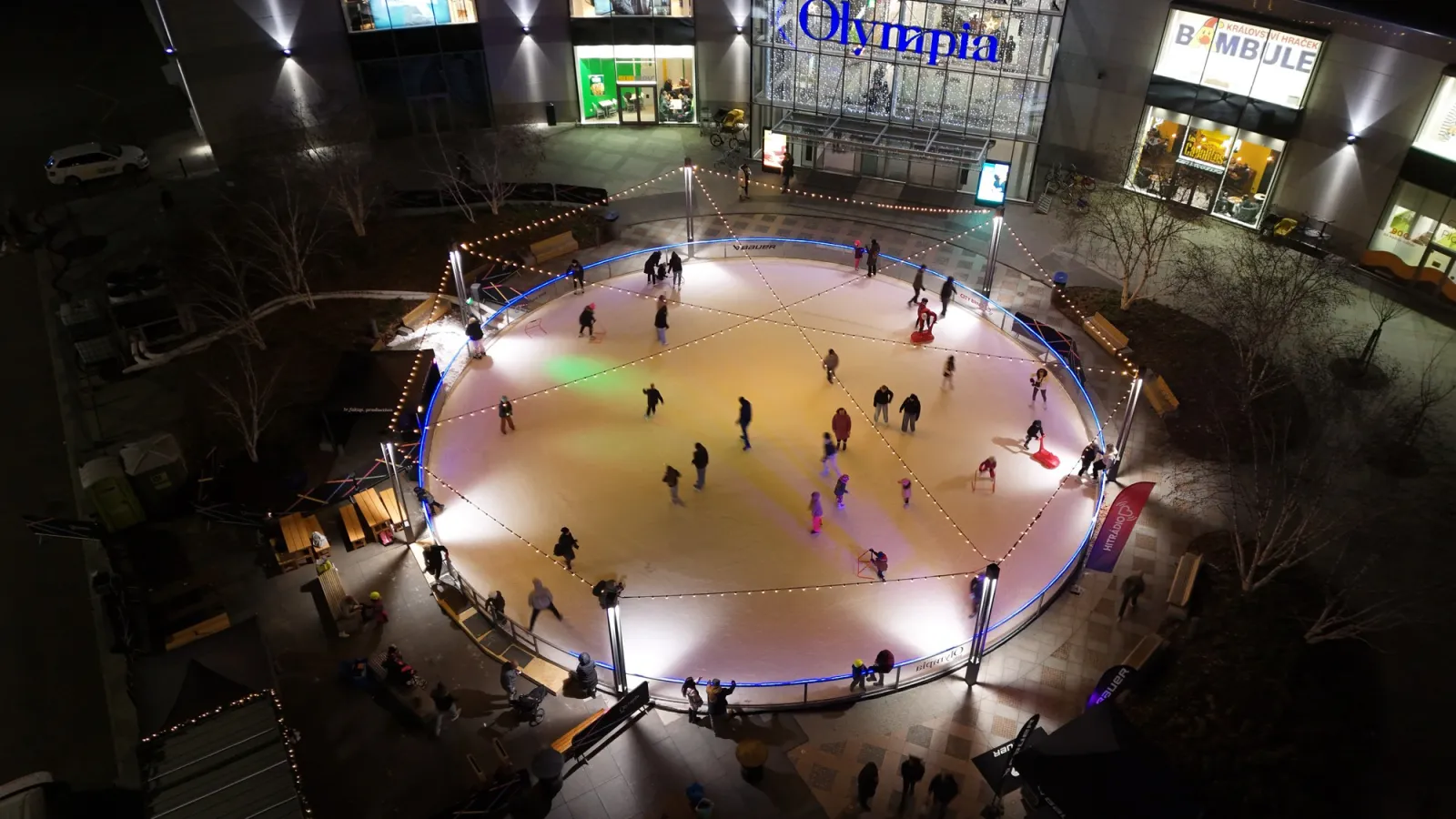 The round ice surface of Olympia Rink seen from above on a skating evening, in front of the Olympia Brno shopping centre — Olympia Rink
