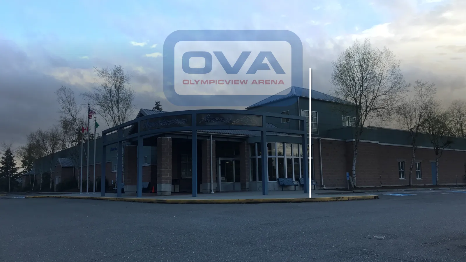 Front entrance of Olympicview Arena, a brick building with a covered walkway and 'Olympicview Arena' signage over the doors, flags flying out front, at dusk — Olympicview Arena