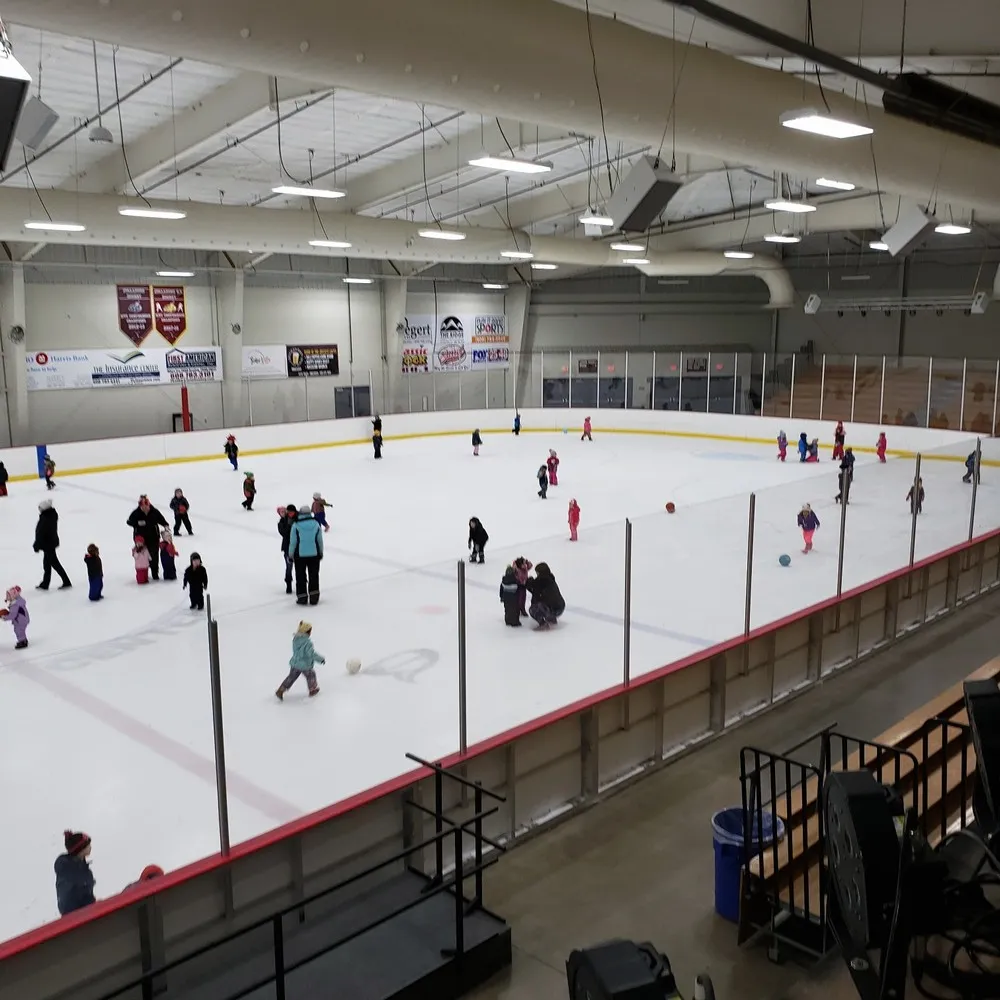 El hielo de la Arena 1 durante un patinaje libre, visto desde las gradas, con patinadores repartidos por la pista y mantas de patrocinadores en la pared del fondo. — Onalaska Omni Center