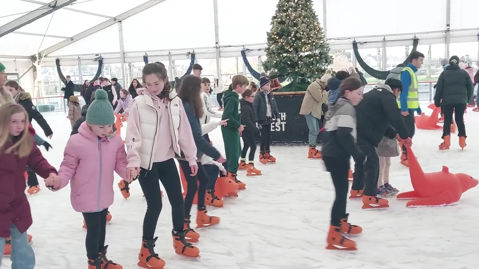 The covered rink under a white tent with the ice surface and a group of skaters at mid-distance; the rink is the subject. — ON ICE Limerick