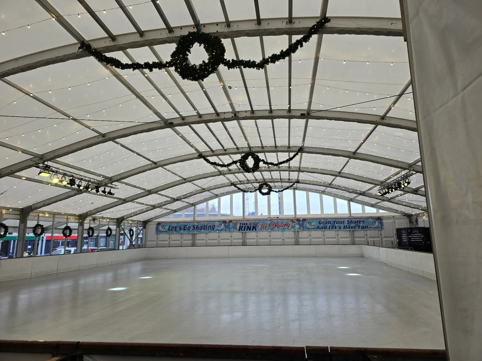 The empty ice inside the ON ICE Waterford marquee with festive wreaths along the arched roof and the Let's Go Skating banner on the far boards — ON ICE Waterford