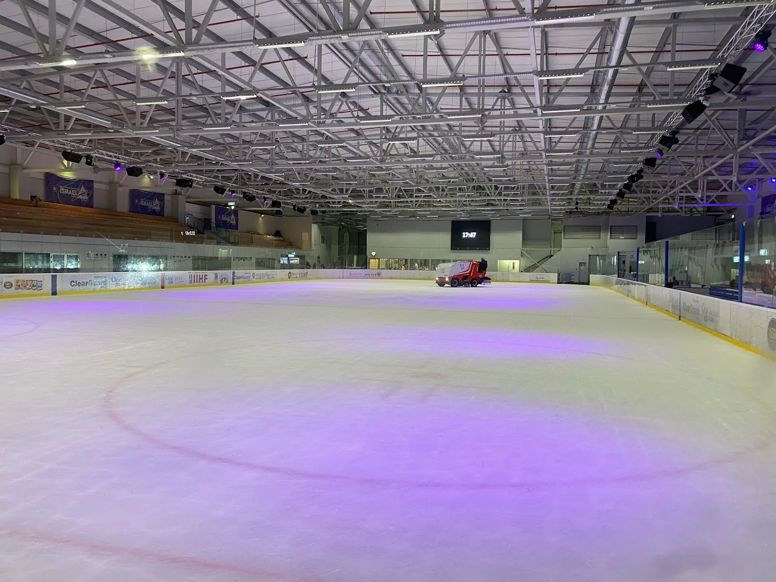 משטח הקרח הריק של OneIce Arena מתחת לגג הפלדה שלה, באור סגול — OneIce Arena