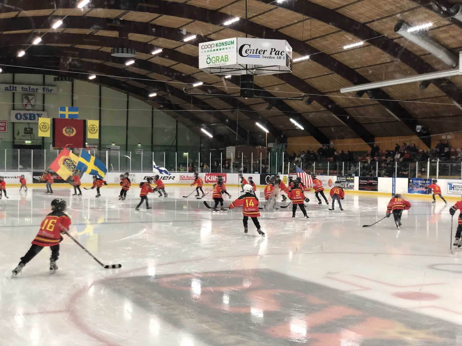 A youth hockey session on the ice of Osby ishall under the curved timber roof with flags along the wall — Osby ishall