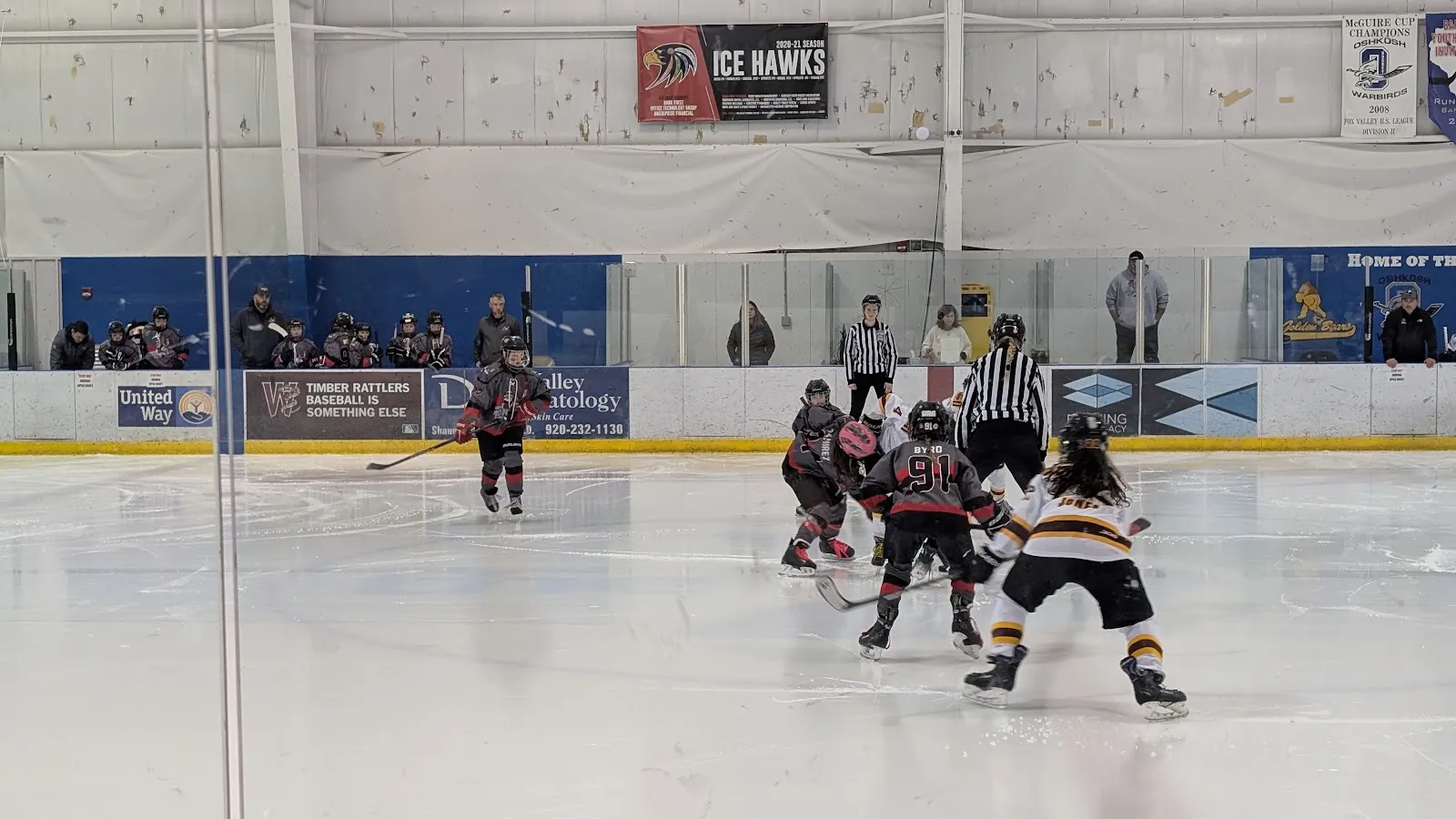 Players in a youth hockey game at the Oshkosh YMCA ice arena, with the boards and arena wall behind. — Oshkosh YMCA Ice Arena